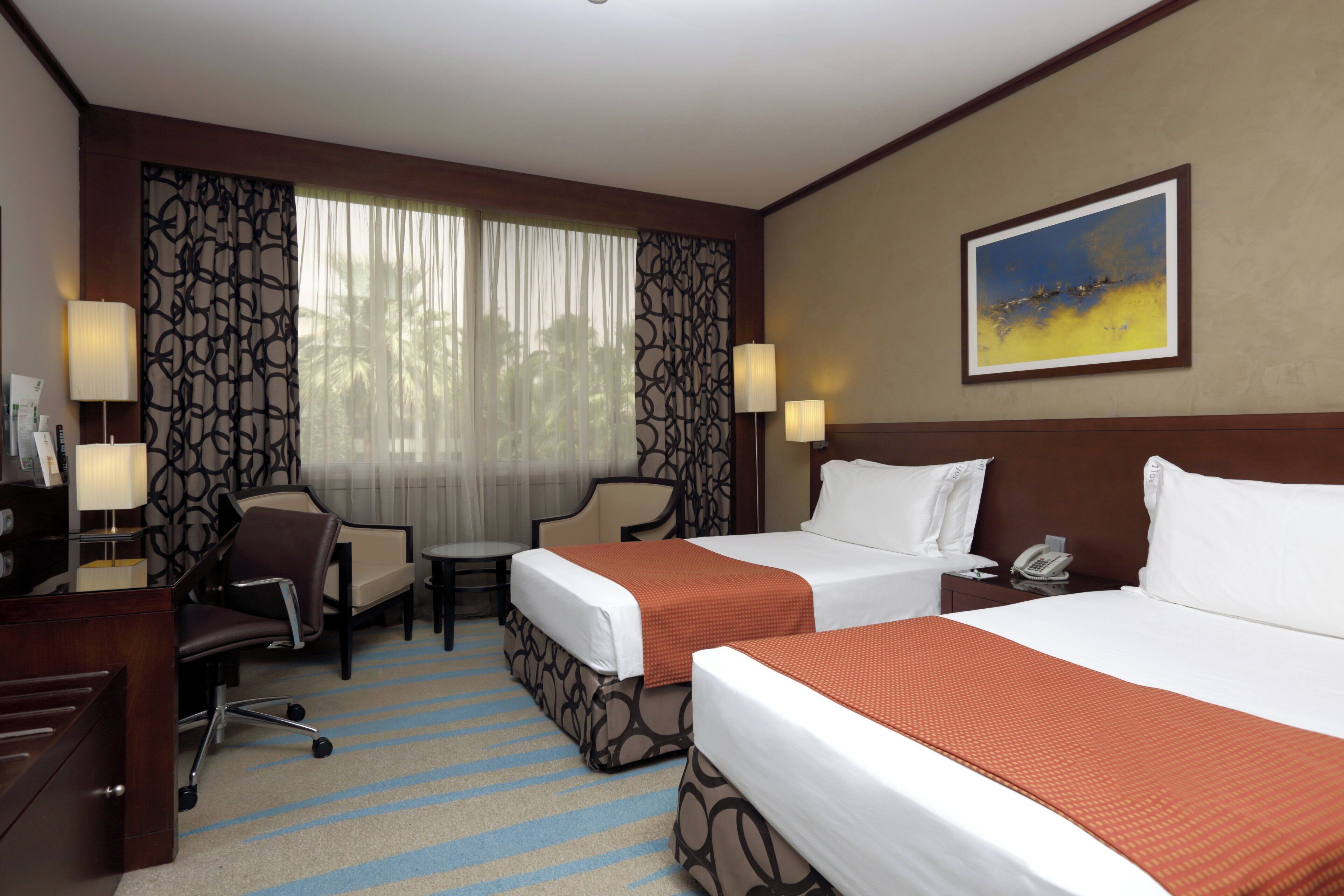 Quarto de hotel com duas camas, uma escrivaninha, uma cadeira, telefone e um quadro na parede.