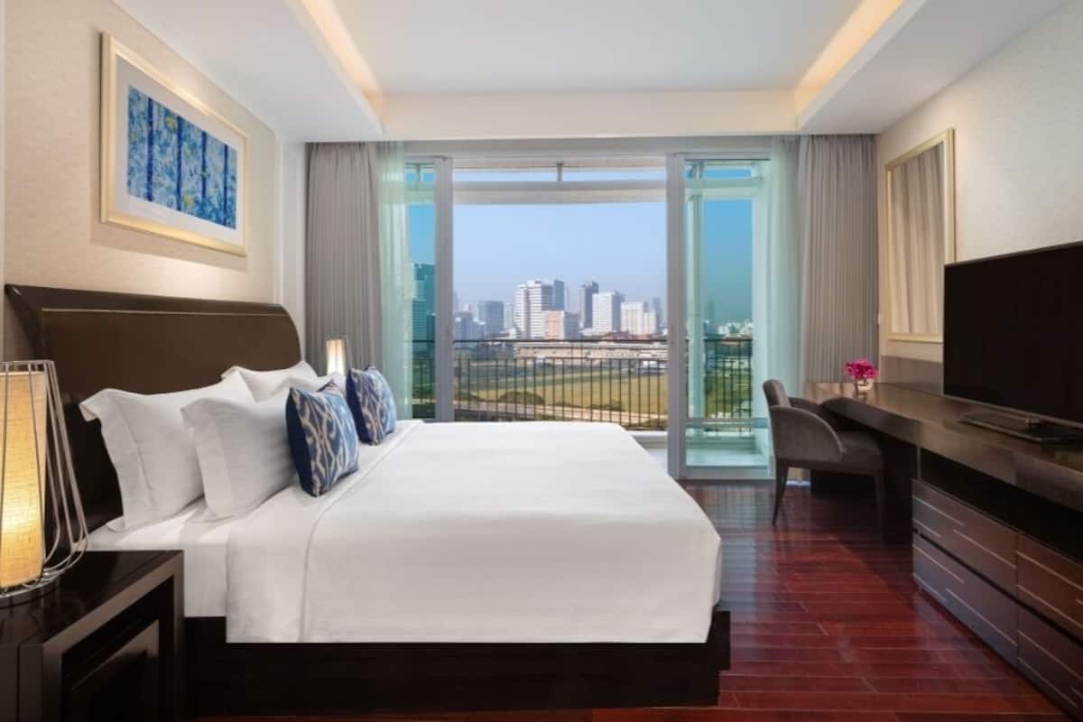 A hotel room with a large bed, a desk, a TV, and a city view through the balcony doors.