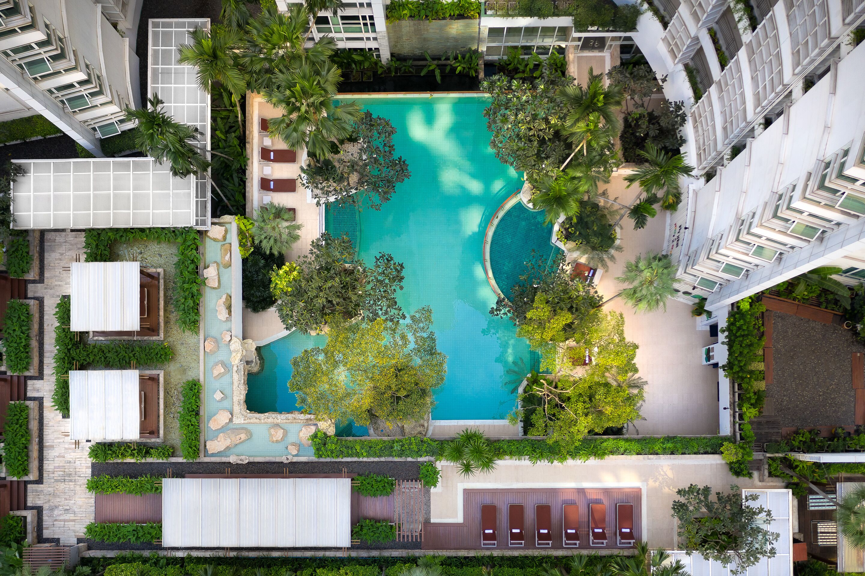 An aerial view of a hotel with a central swimming pool surrounded by lush greenery and multiple buildings.