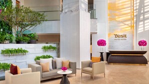 A modern hotel lobby with a reception desk, sofas, and potted plants.