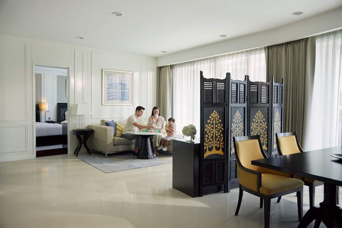 A modern hotel room with a dining area, a sofa set, and a decorative screen.
