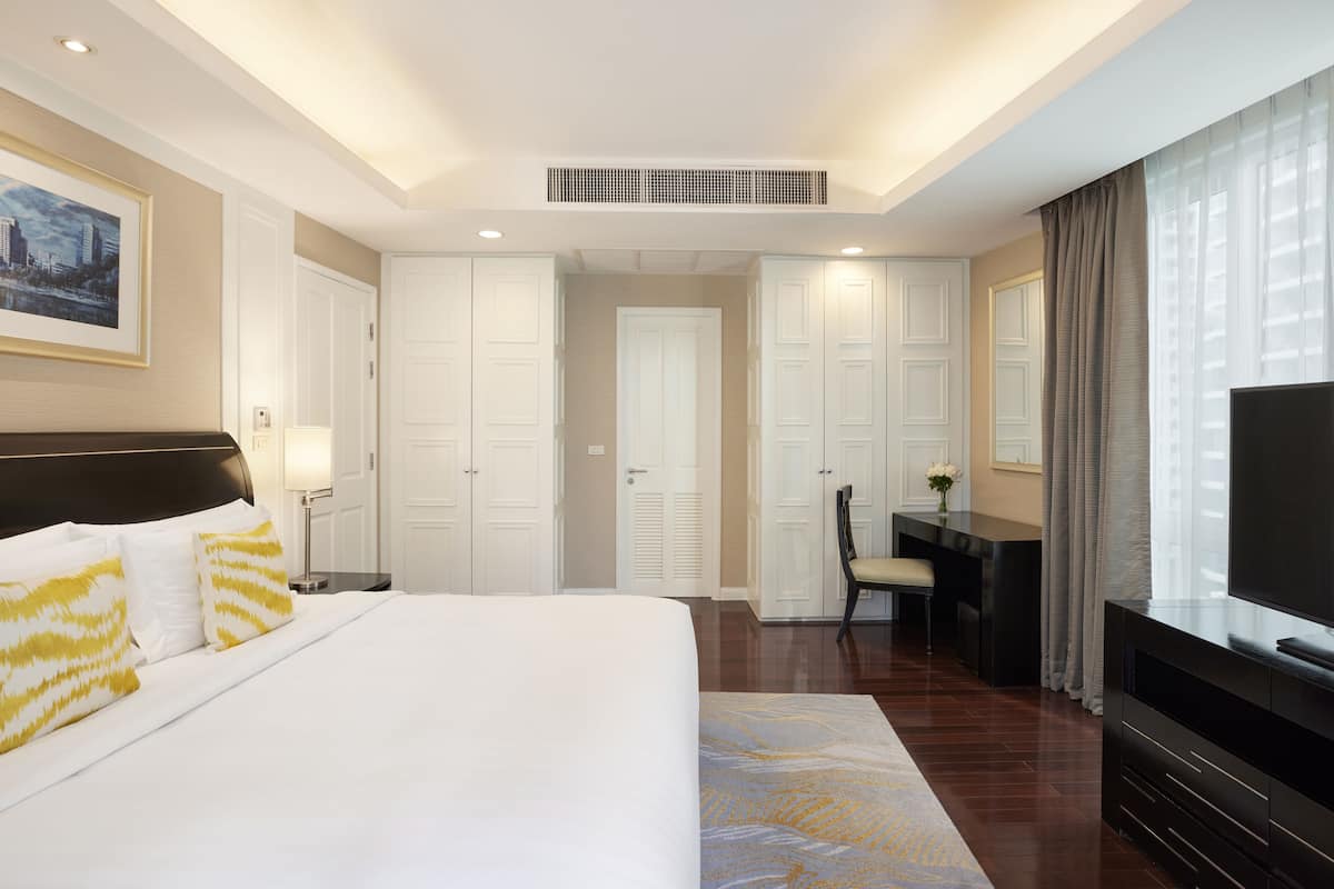 A hotel room with a large bed, a desk, a chair, a television, and a wardrobe.