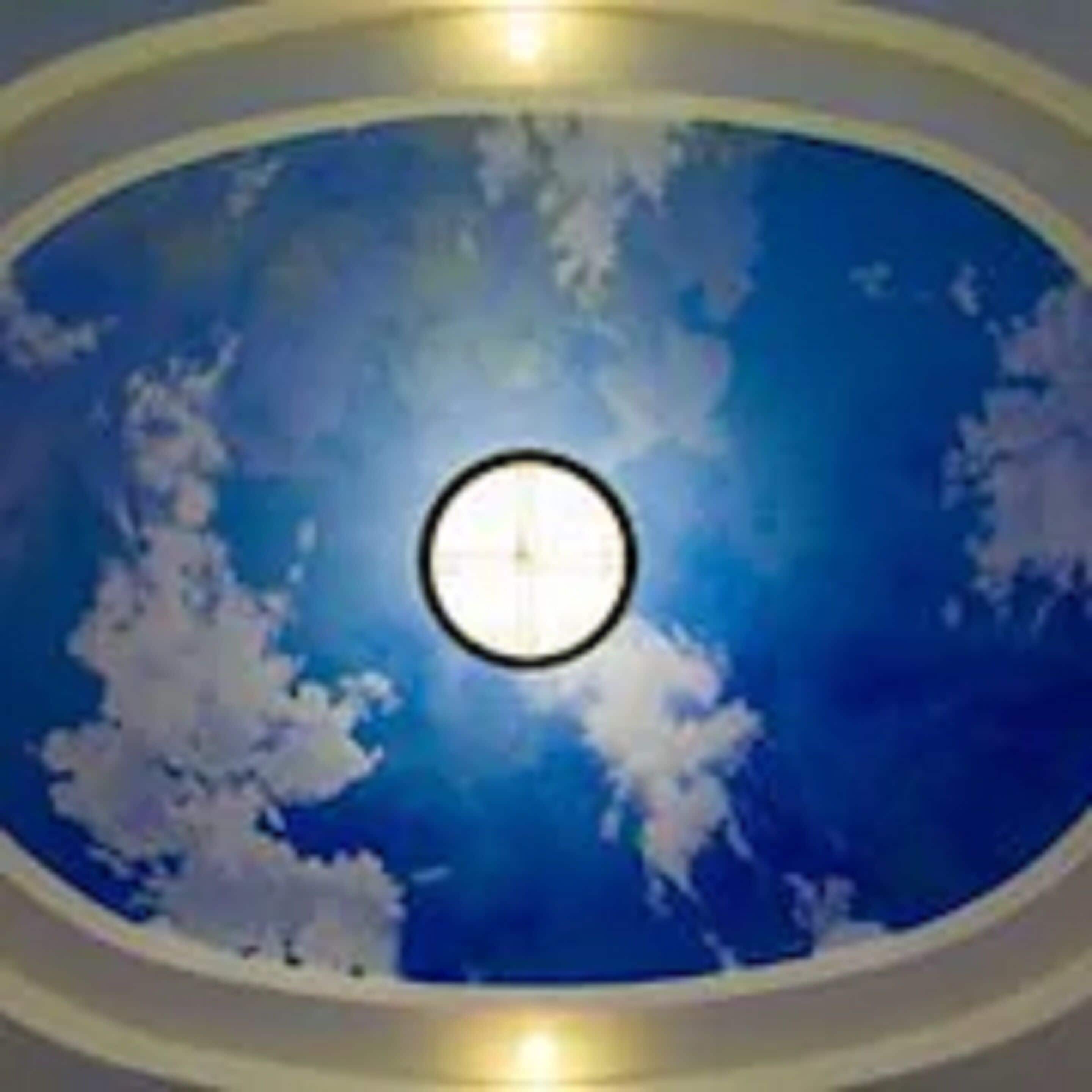 A circular skylight with a sun-like design, surrounded by a blue sky with clouds.