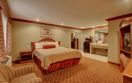 A hotel room with a large bed, a desk, a chair, a dresser, and a bathroom visible through an open door.