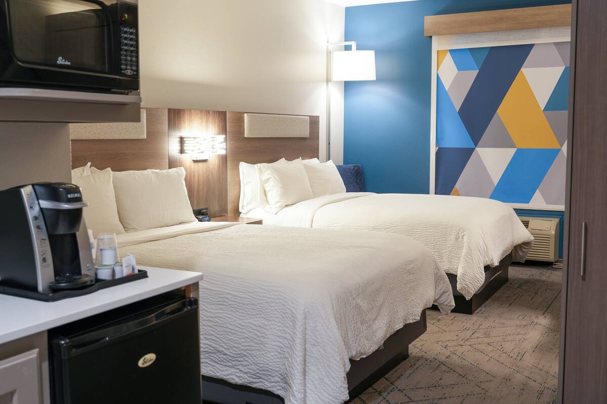 A hotel room with two beds, a microwave, a coffee maker, and a wall with a geometric pattern.
