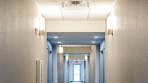 Un couloir d’hôtel avec un tapis à motifs, des luminaires encastrés et une porte au bout.