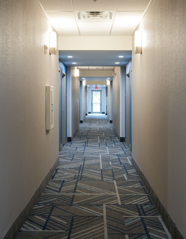 Ein Hotelgang mit strukturiertem Teppichboden, eingelassener Beleuchtung und einer Tür am Ende.