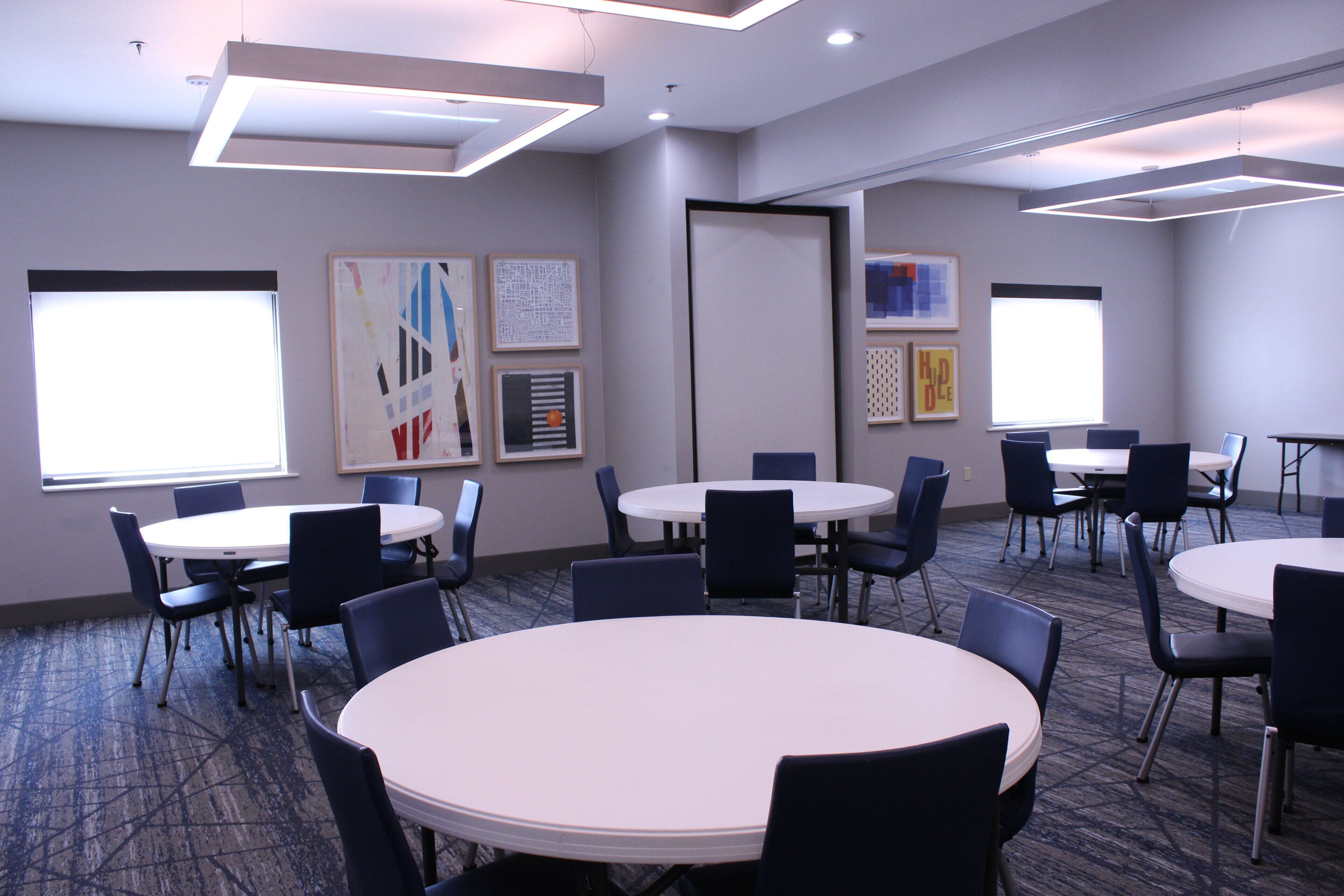 A conference room with round tables and chairs, framed artwork on the walls, and a carpeted floor.
