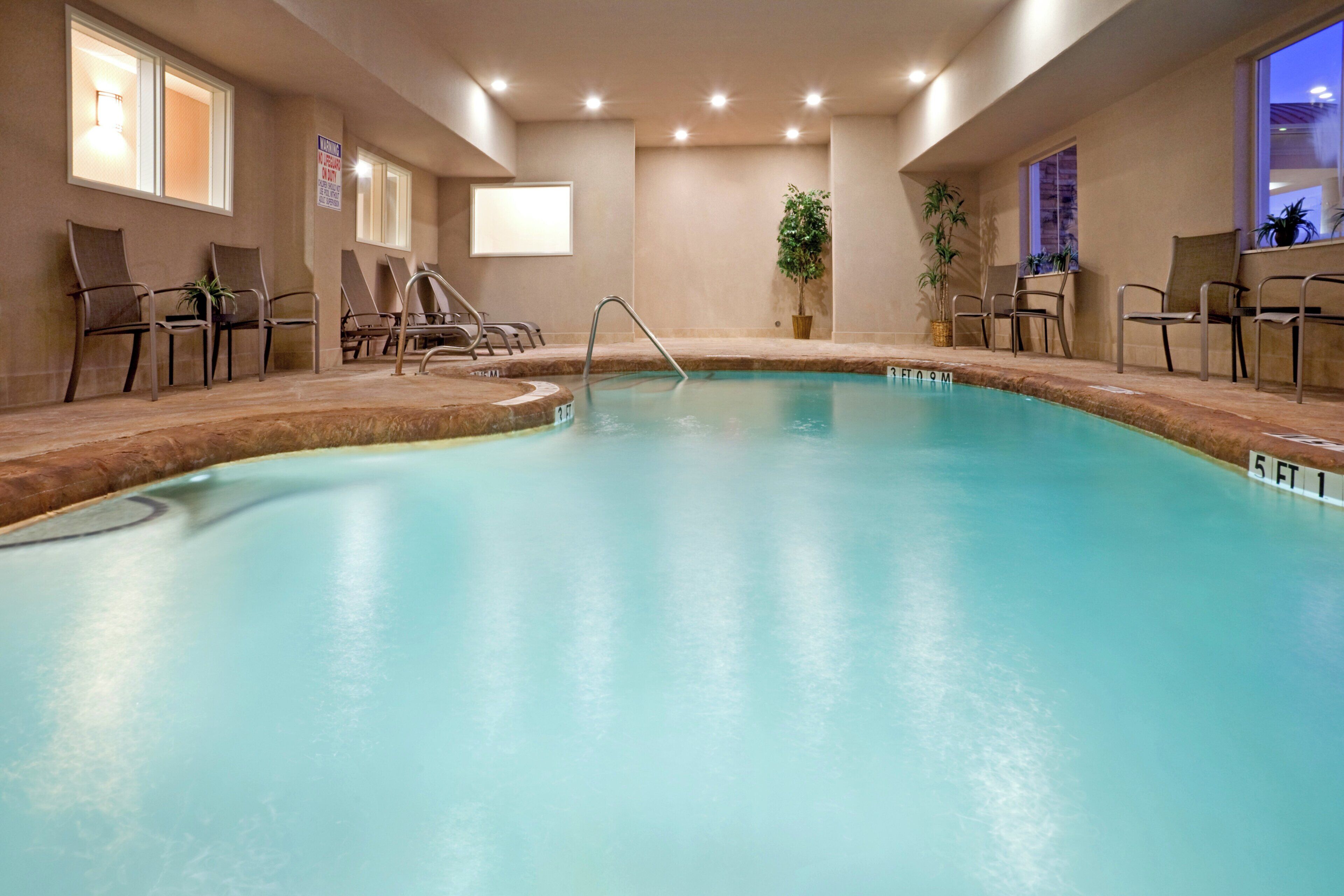 An indoor swimming pool with a diving board, lounge chairs, and a potted plant.