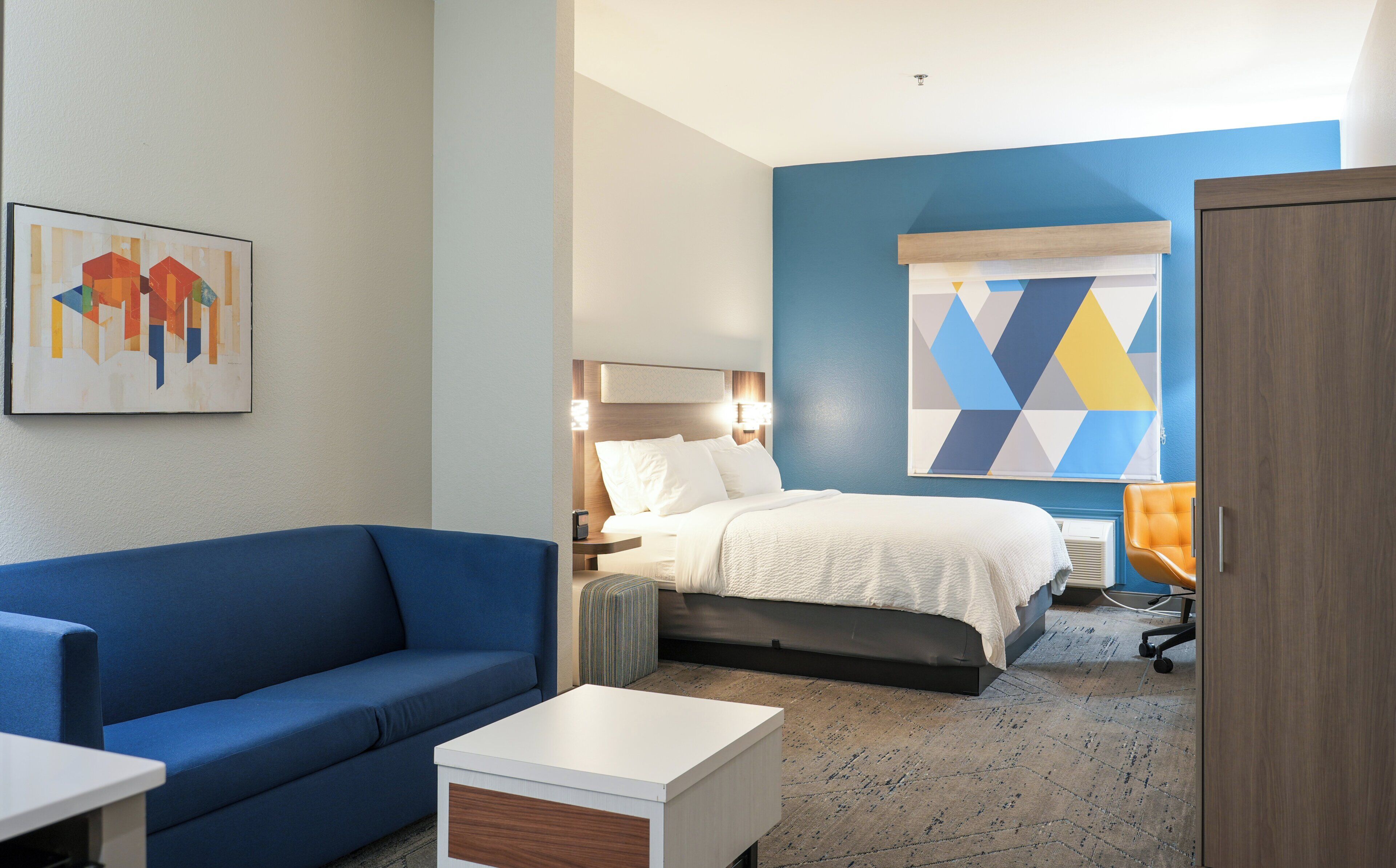 A hotel room with a bed, a blue sofa, a small table, and a painting on the wall.