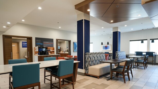 Un hall d’hôtel moderne avec une longue table à manger, plusieurs chaises, un canapé et un coin café.