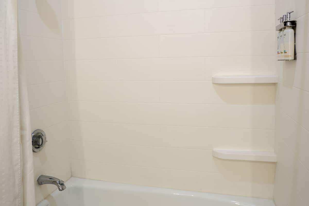 A bathroom with a bathtub, a showerhead, and a soap dispenser on a wall.