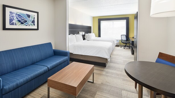 A hotel room with a blue sofa, a wooden coffee table, a bed with white linens, a desk with a chair, and a large window. - Holiday Inn Express Hotel & Suites Spartanburg-North by IHG (Spartanburg)