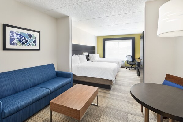 A hotel room with a blue sofa, a wooden coffee table, a bed with white linens, a desk with a chair, and a large window. - Holiday Inn Express Hotel & Suites Spartanburg-North by IHG (Spartanburg)