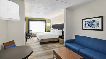 A hotel room with a bed, a blue sofa, a wooden table, a lamp, and a framed abstract painting on the wall.