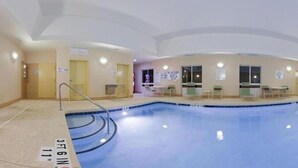 Una amplia piscina interior con trampolín, varias puertas y zonas de estar.