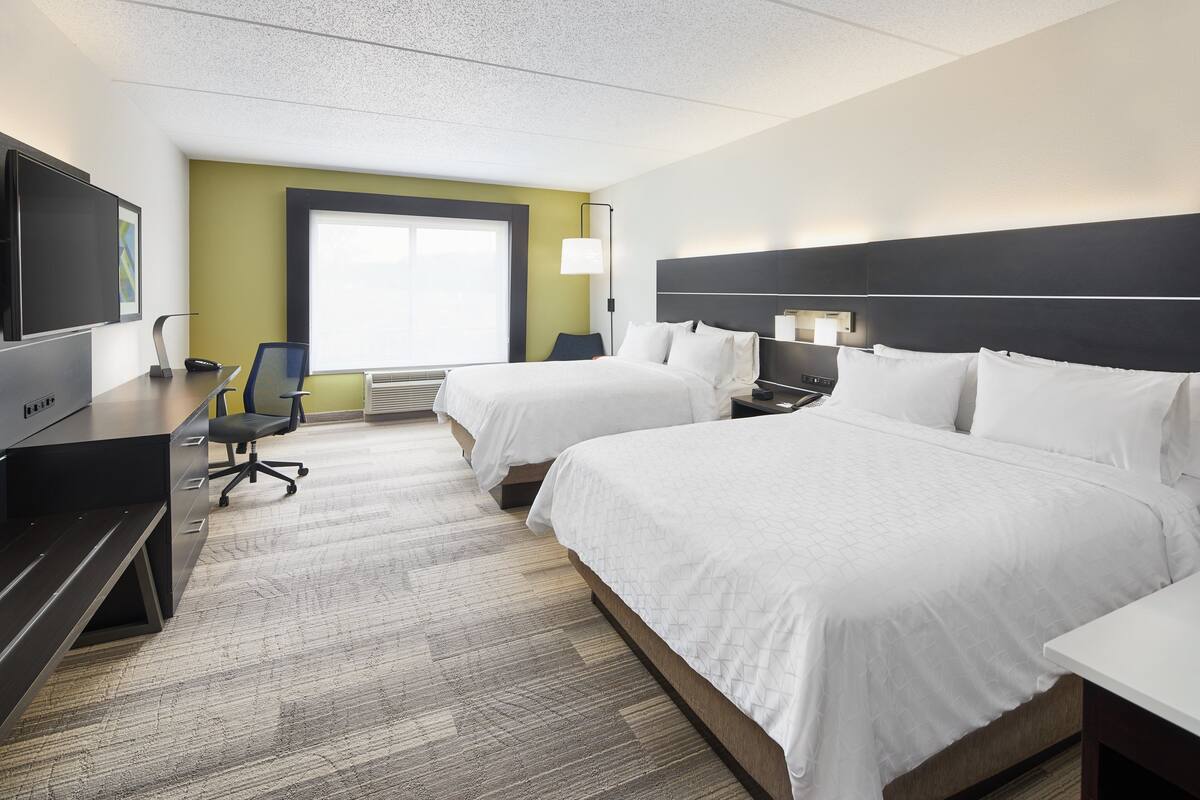 A hotel room with two beds, a desk with a chair, a television, and a large window.