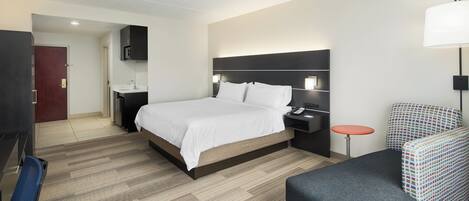 Une chambre d’hôtel comprenant un lit, une table de chevet, une lampe, une chaise et un bureau avec une autre chaise.