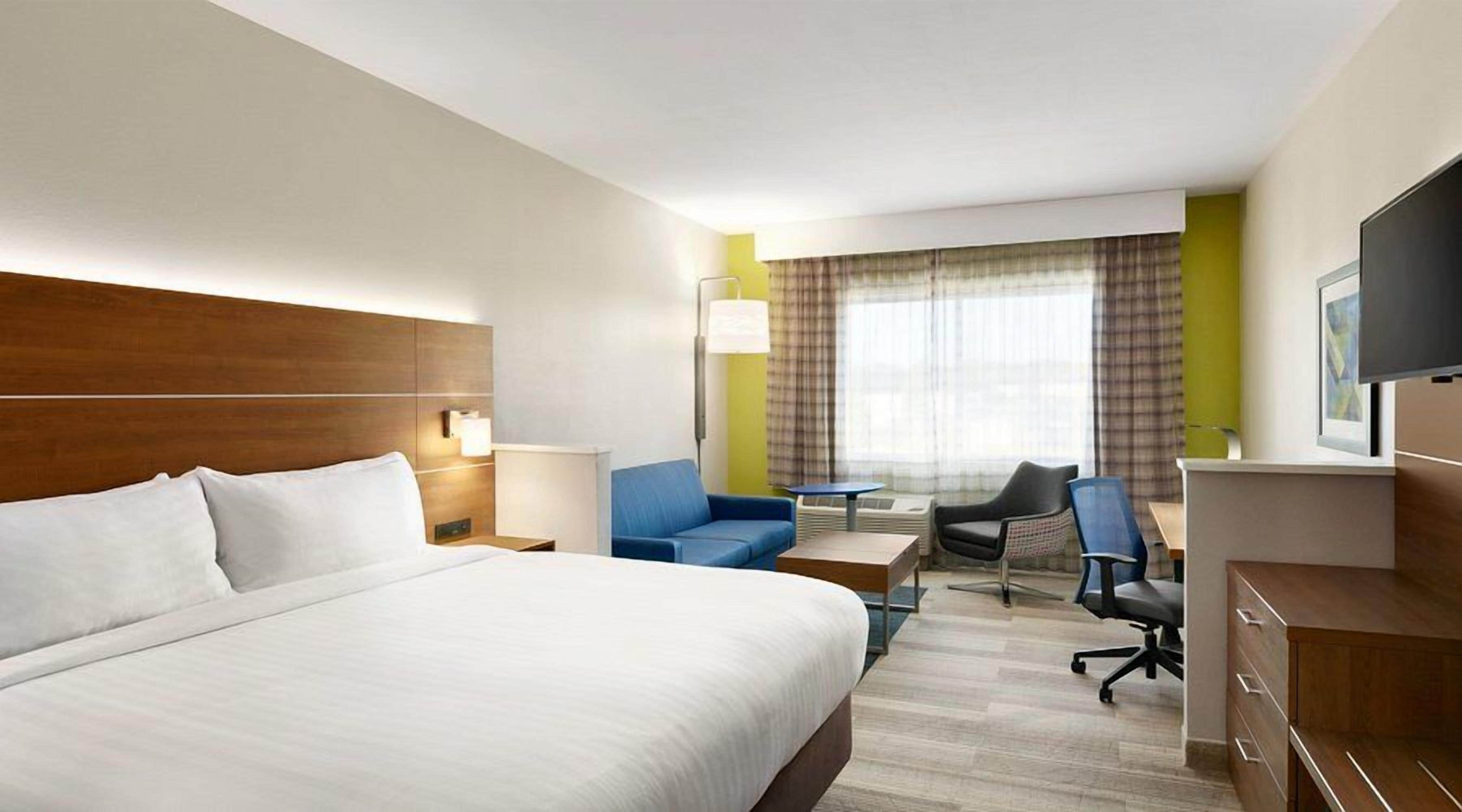A hotel room with a large bed, a desk, a chair, a television, and a window with curtains.