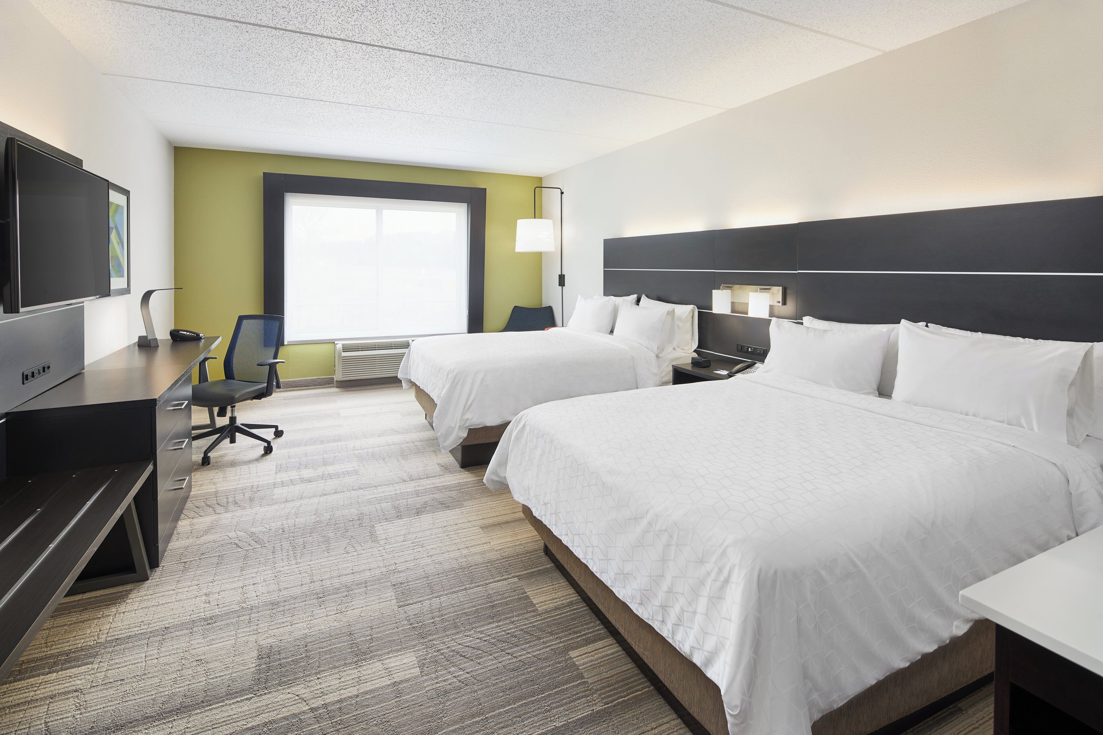 A hotel room with two beds, a desk, a chair, a TV, and a window.
