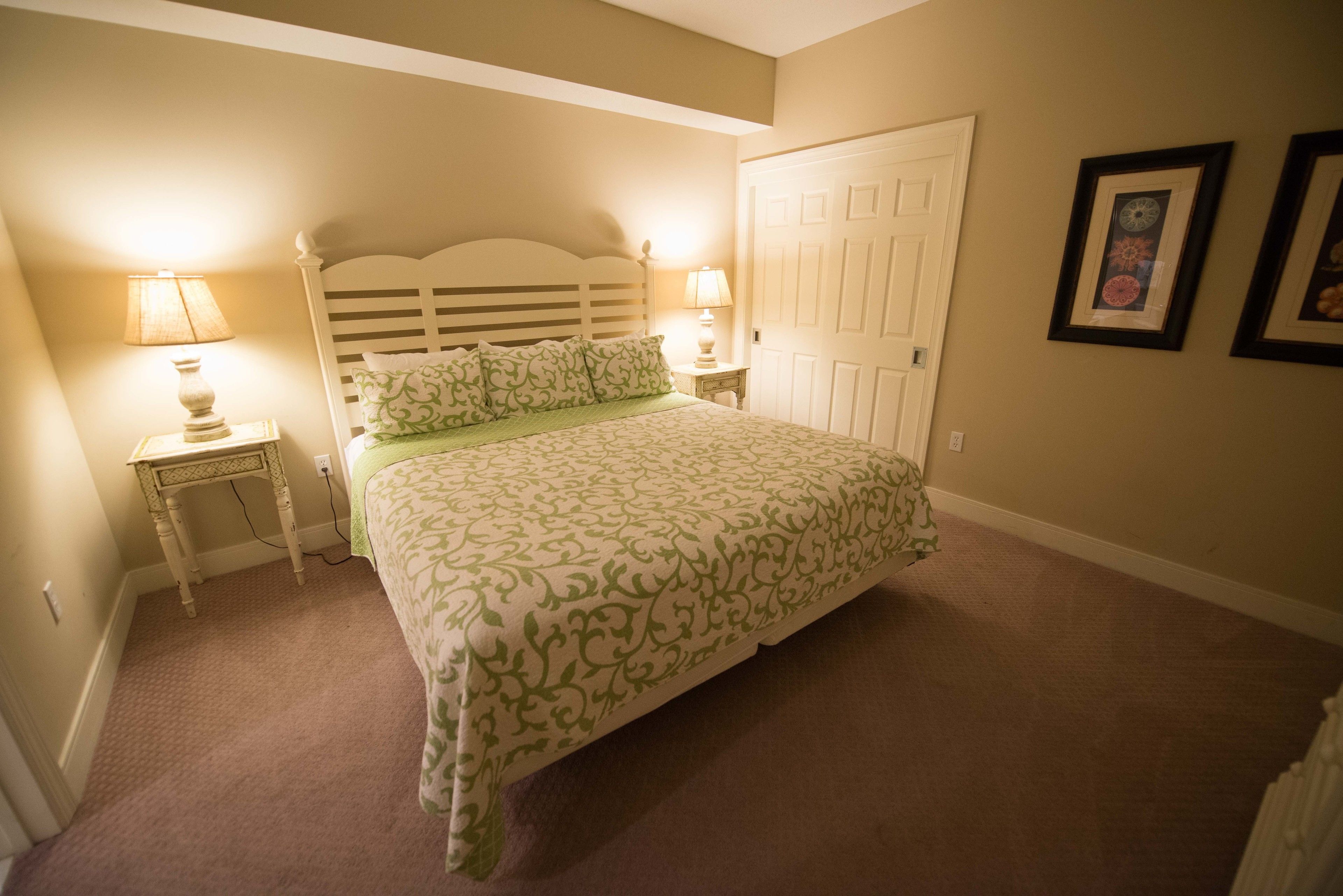 A bedroom with a bed, two bedside lamps, a door, and two framed pictures on the wall.