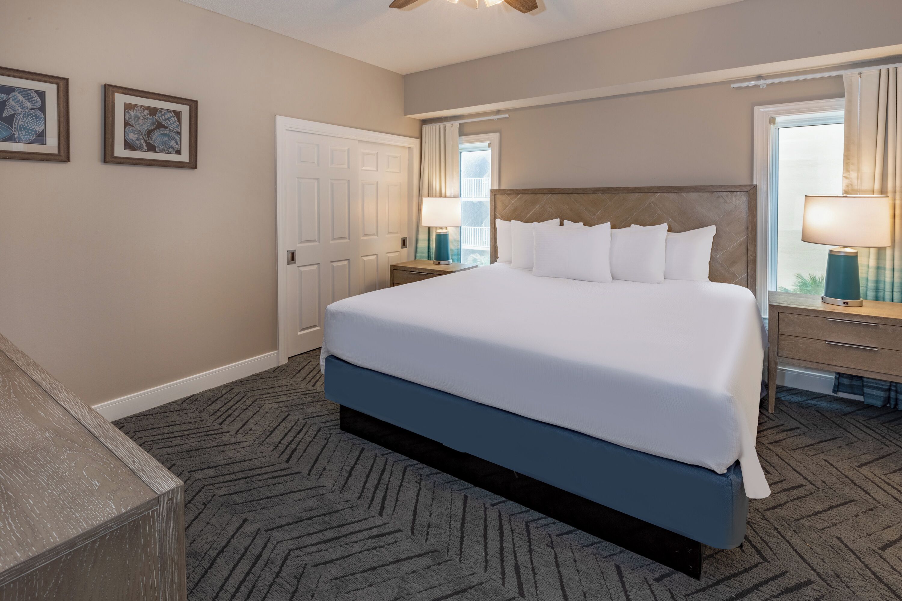 A hotel room with a large bed, a nightstand with a lamp, a dresser, and a door.