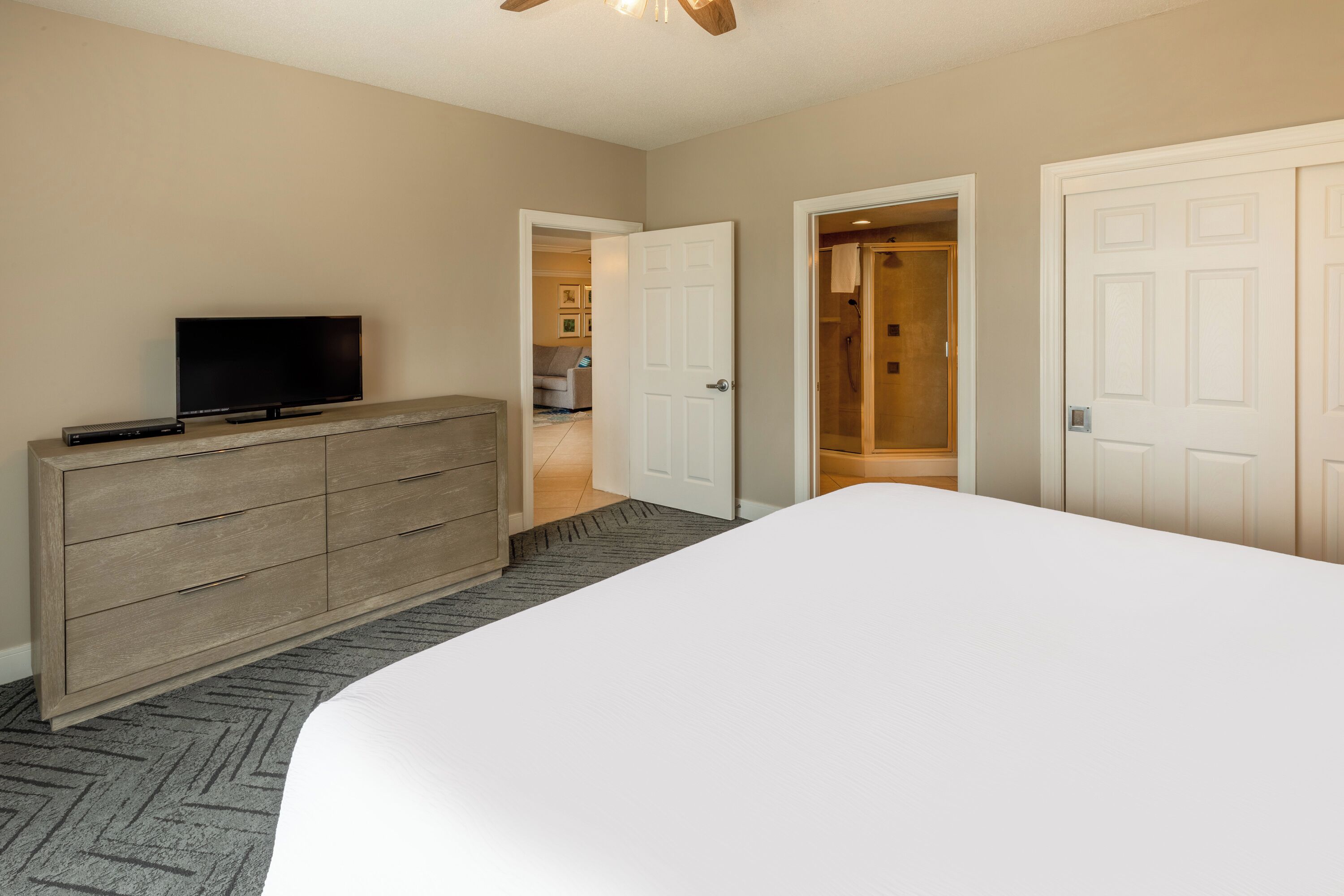 Camera d'albergo con un letto grande, un comò in legno, una TV a schermo piatto e due porte che conducono ad altre stanze.