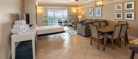 Une chambre d’hôtel comprenant un lit, une table à manger avec des chaises, un canapé, une télévision et un balcon avec vue sur l’océan.