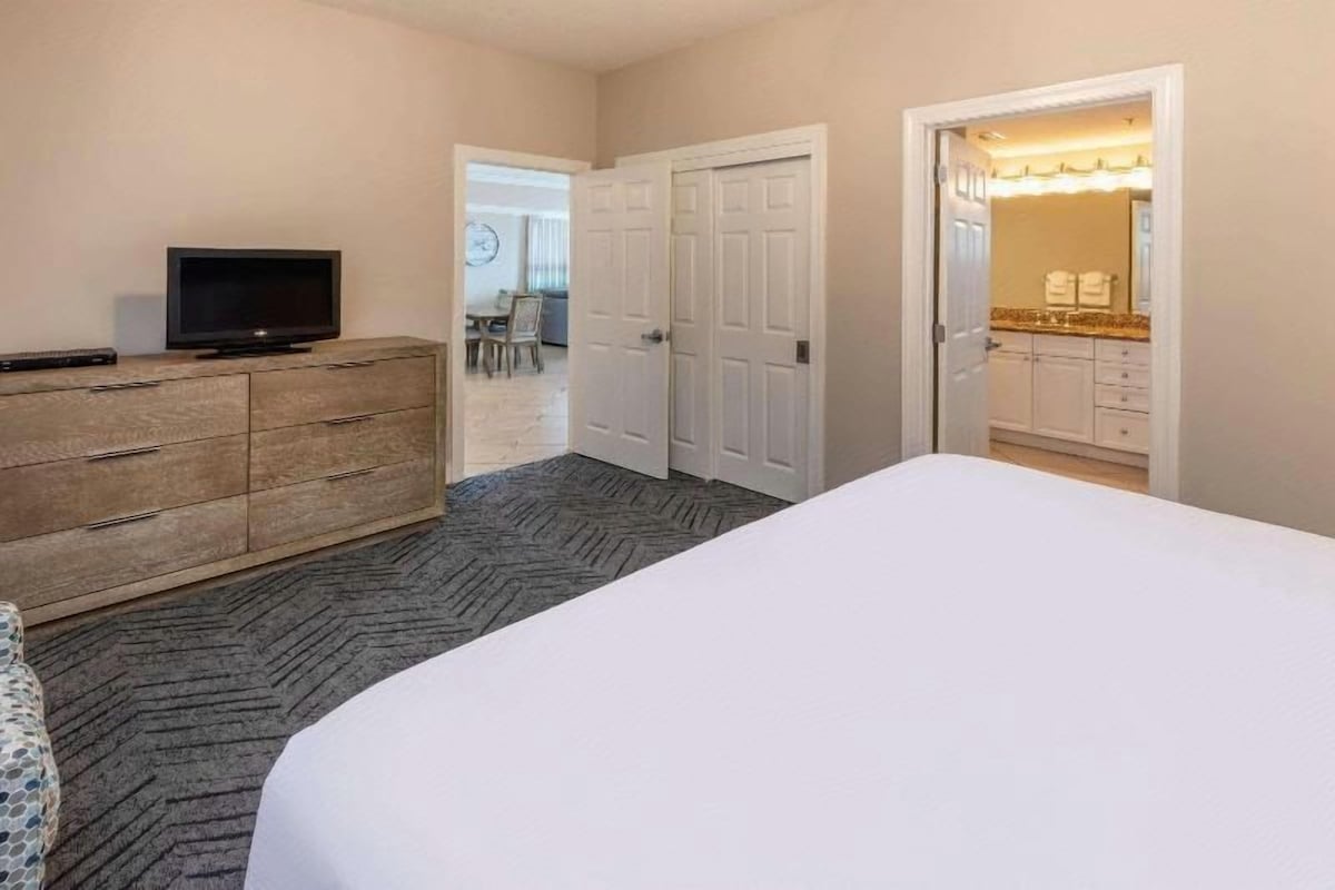 Une chambre d’hôtel avec un lit, une commode, un téléviseur et une salle de bain visible à travers une porte ouverte.
