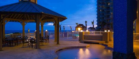 A pool area with a gazebo, lounge chairs, and a view of the ocean at dusk.