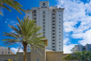 A tall hotel with a prominent 'Escapesi' sign, featuring a modern architectural design with multiple balconies and a clear view of the sky.