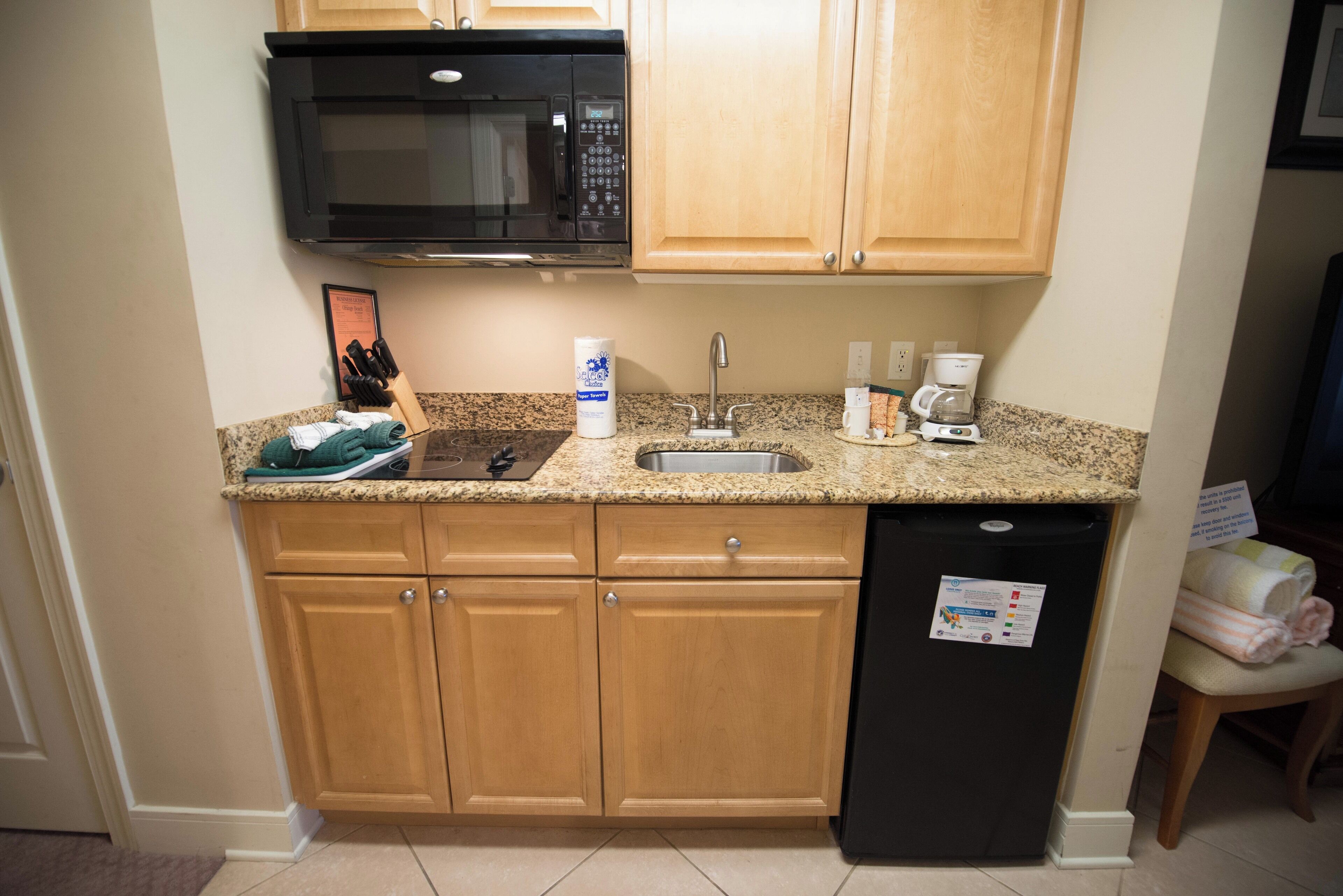 A compact kitchen with wooden cabinets, a built-in microwave, a sink, and a refrigerator.