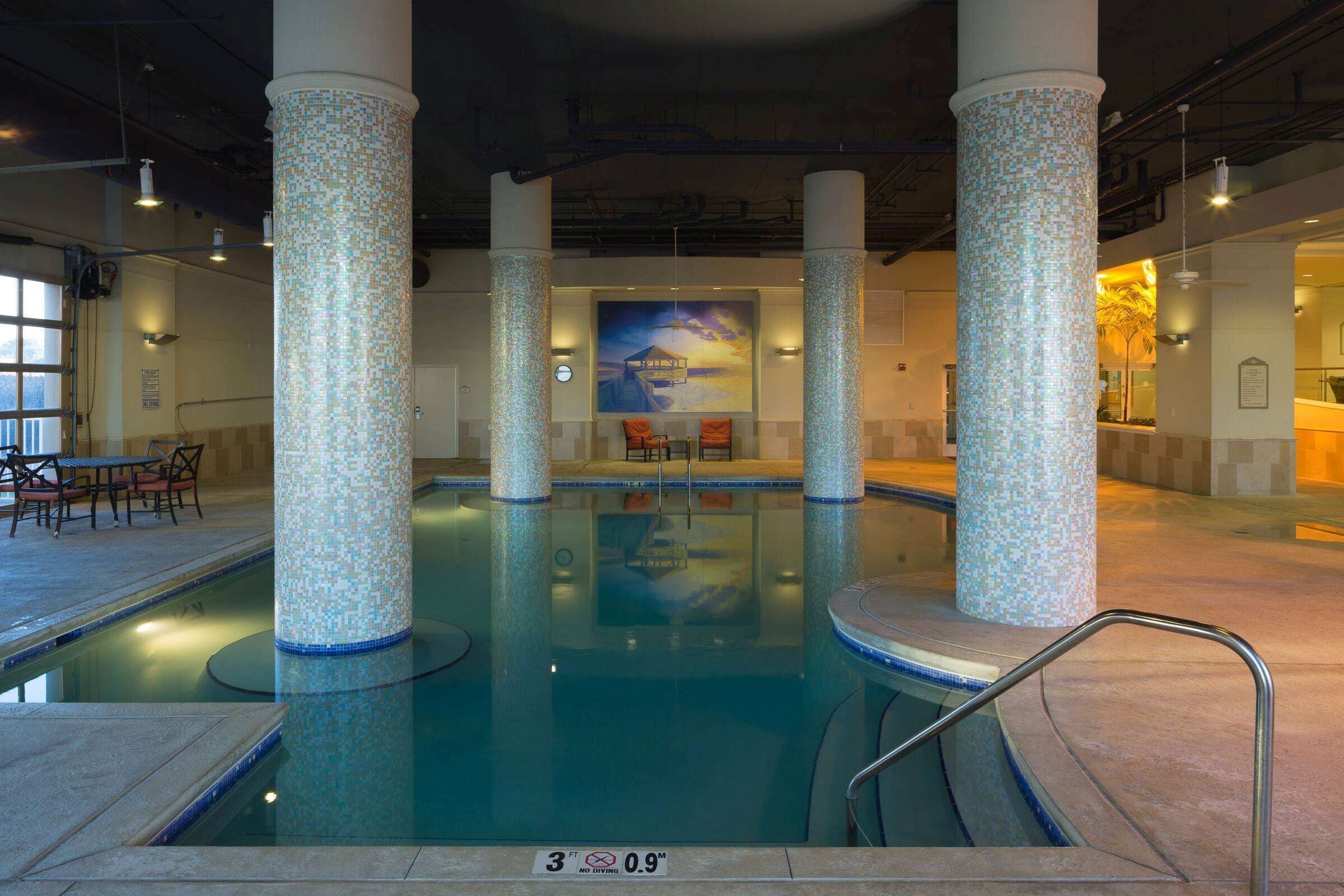 Ein Innenpool mit mosaikverzierten Säulen, einer Sitzecke und einem Wandgemälde an der Rückwand.
