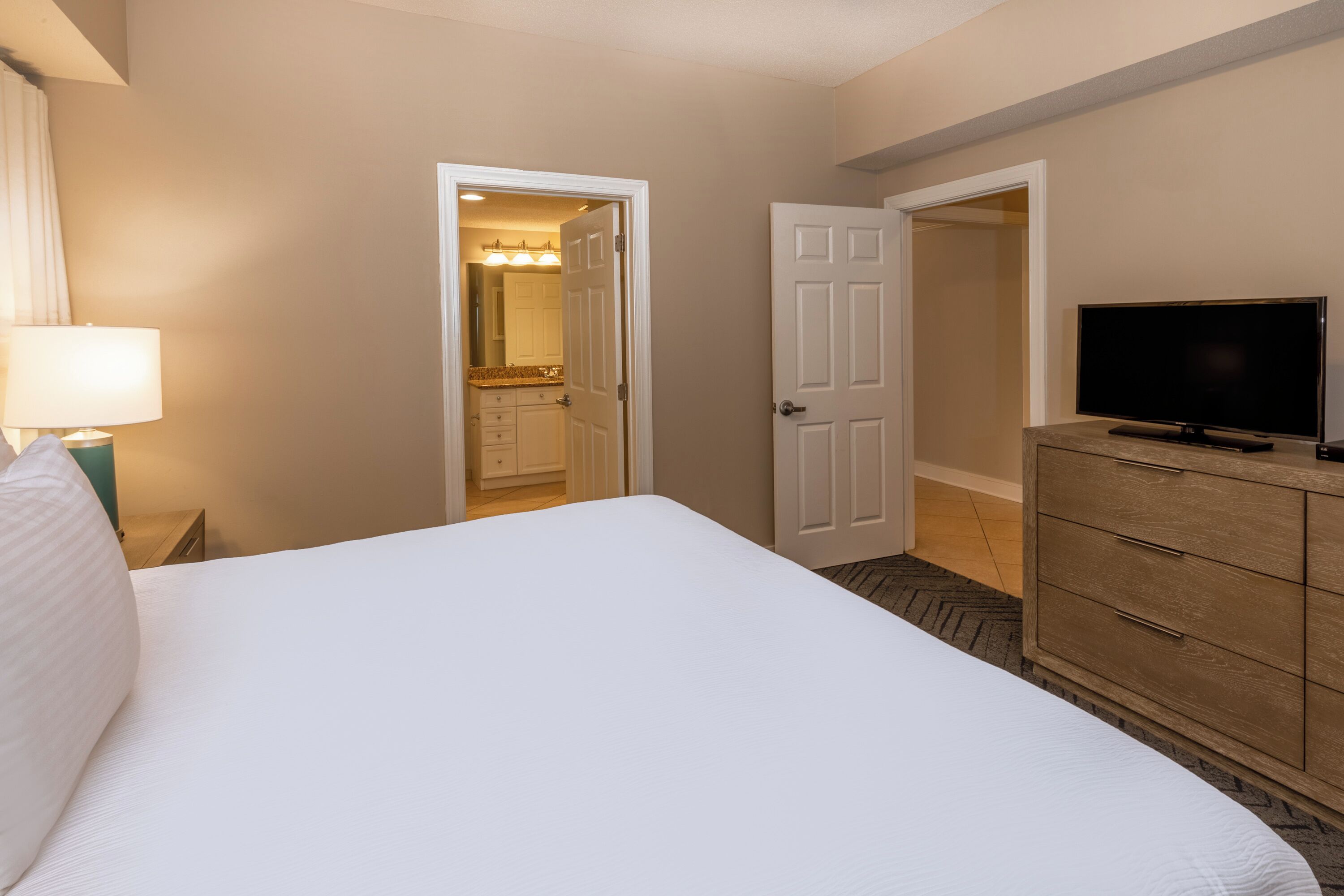 Habitación de hotel con una cama grande, un televisor sobre un aparador de madera y un baño visible a través de una puerta abierta.