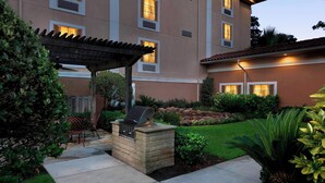 Un patio con una parrilla, mobiliario exterior y una pérgola.