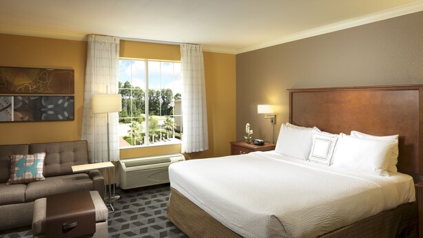 Una habitación de hotel con una cama grande, un sofá, una mesita y una ventana con cortinas.