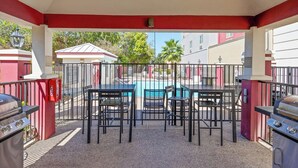 An outdoor patio with a pool, tables, chairs, and barbecue grills. - Candlewood Suites San Antonio Downtown by IHG (San Antonio)