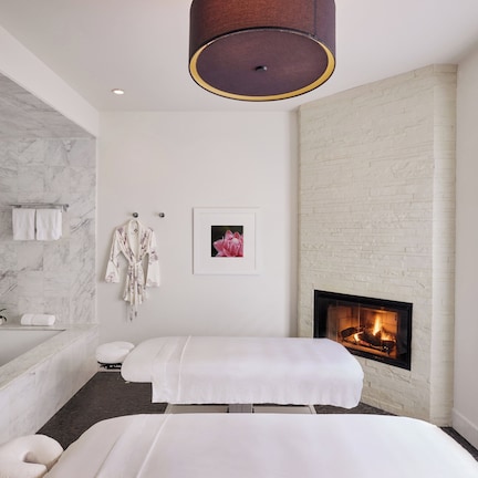 A modern bathroom with a marble shower, a bathtub, a large mirror, and a fireplace.