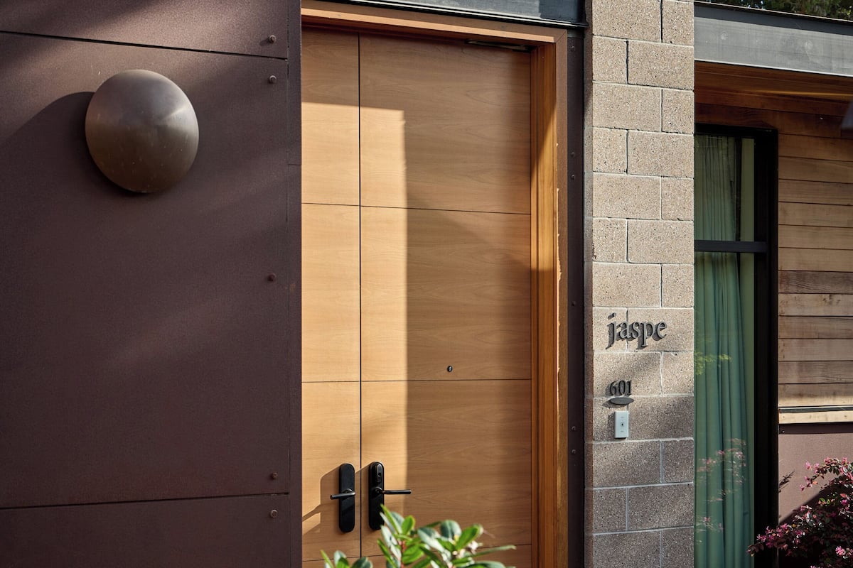 Un edificio moderno con una puerta de madera, una pared de piedra y una ventana con cortina verde.