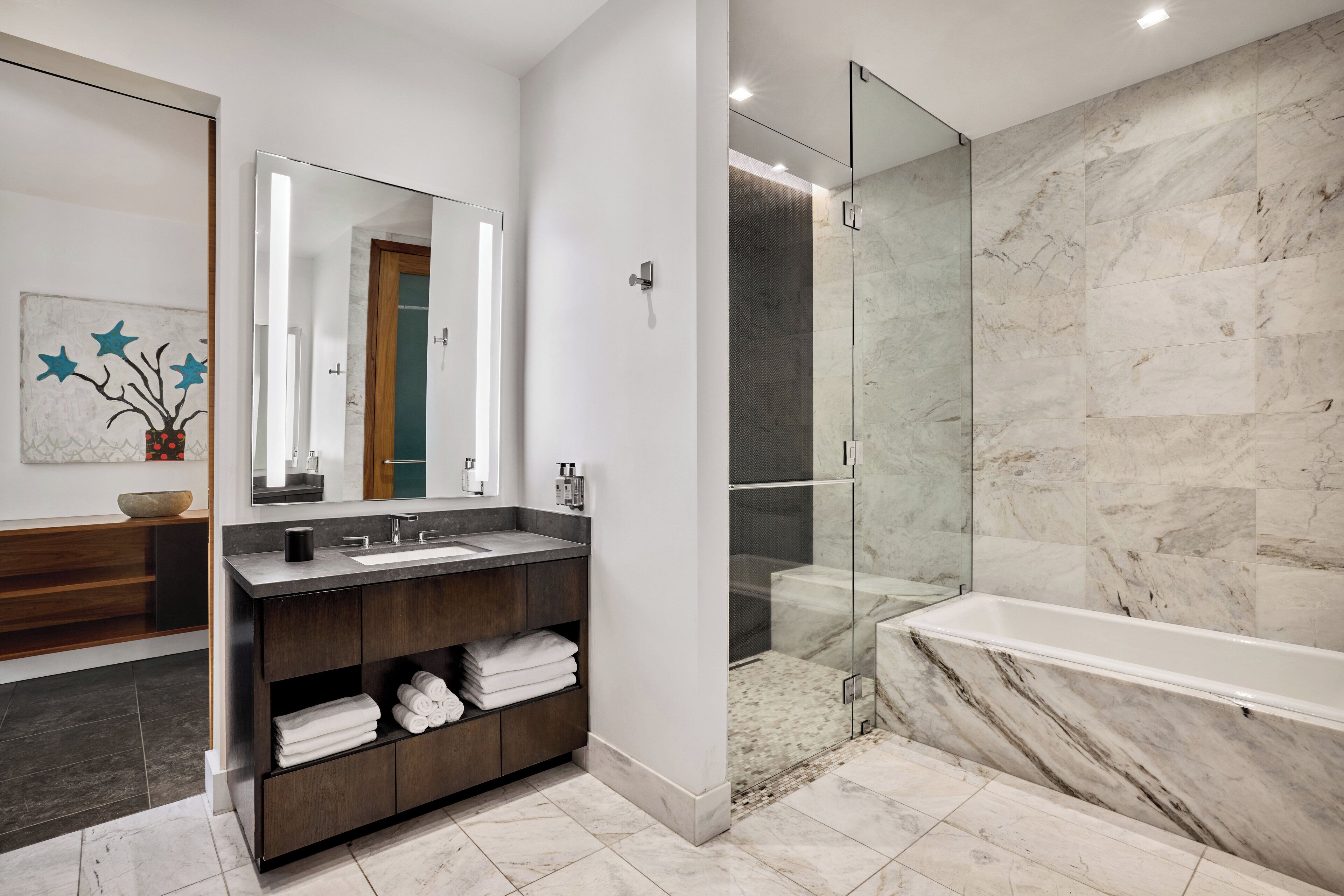 Un baño moderno con ducha de vidrio, un espejo grande y una bañera de mármol.