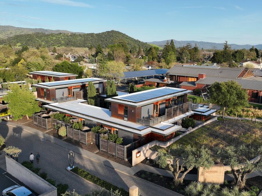Zona residencial con casas modernas de techos planos y paneles solares, rodeada de vegetación y colinas al fondo.