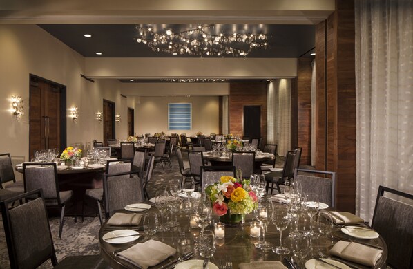 Un amplio salón de banquetes con varias mesas redondas dispuestas para cenar, con vasos transparentes y centros de mesa.