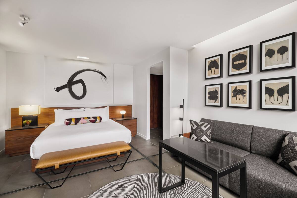 Una habitación de hotel moderna con una cama grande, un sofá, una mesa de centro y obras de arte en las paredes.