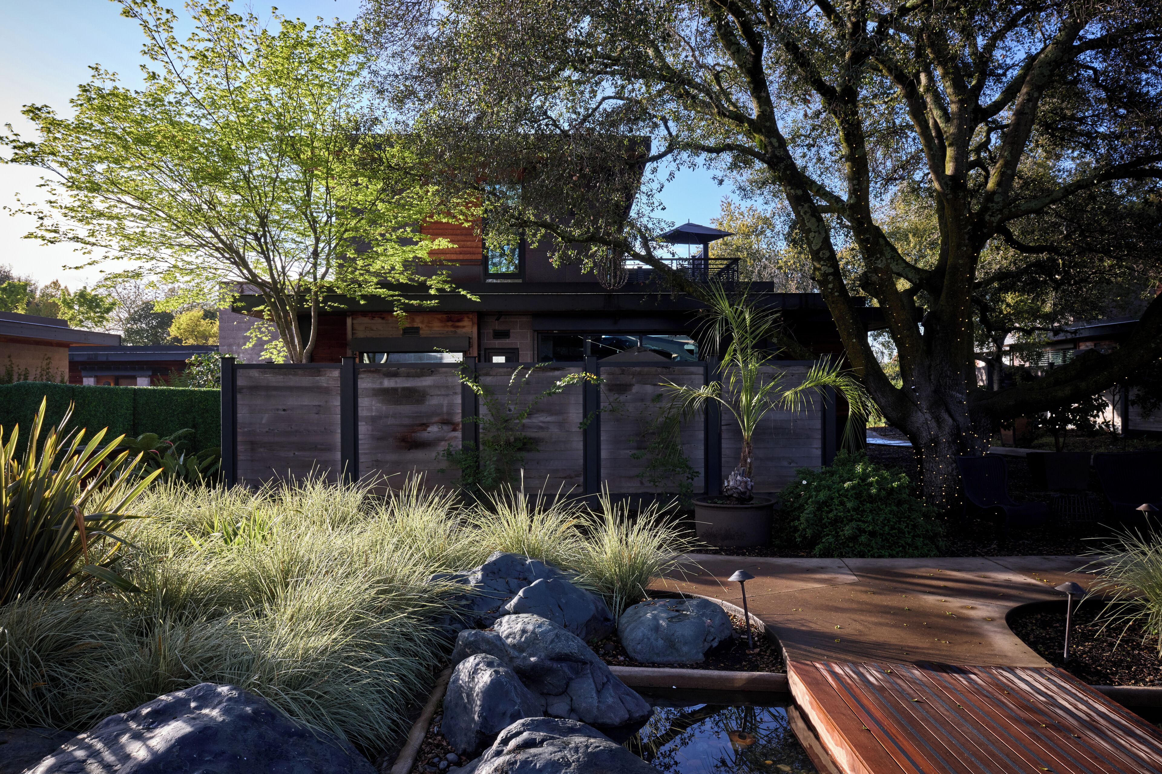 Una casa moderna con terraza de madera, un sendero de piedra y un pequeño estanque.