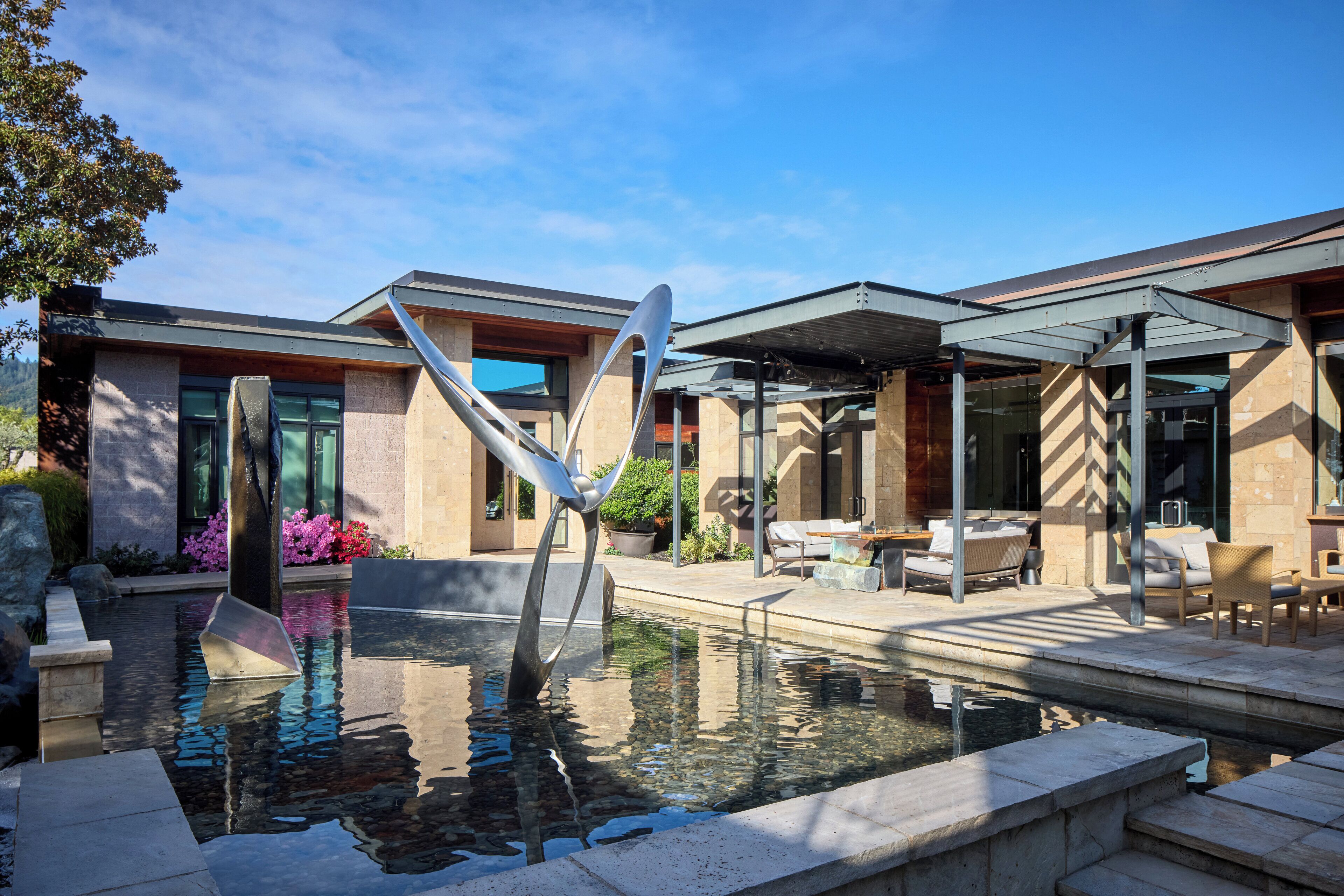 Un área de piscina moderna con una escultura metálica única, asientos exteriores y vistas despejadas a la piscina.