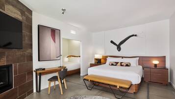 Et moderne hotelværelse med en stor seng, et skrivebord, en stol, et fjernsyn, en pejs og et kunstværk på væggen.