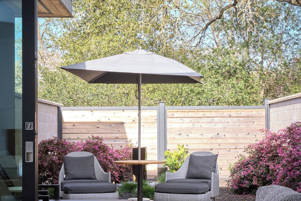 Un patio al aire libre con dos sillones grises, un sofá de mimbre trenzado y una mesa de madera.