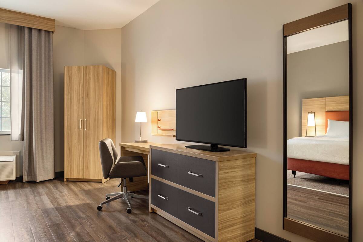 Een hotelkamer met een houten bureau, een televisie, een stoel, een bed en een grote spiegel.