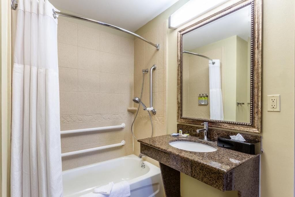 A bathroom with a bathtub, a sink, a mirror, and a shower with grab bars.