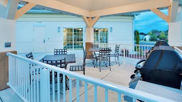 An outdoor patio with a grill, tables, and chairs, overlooking a residential area.